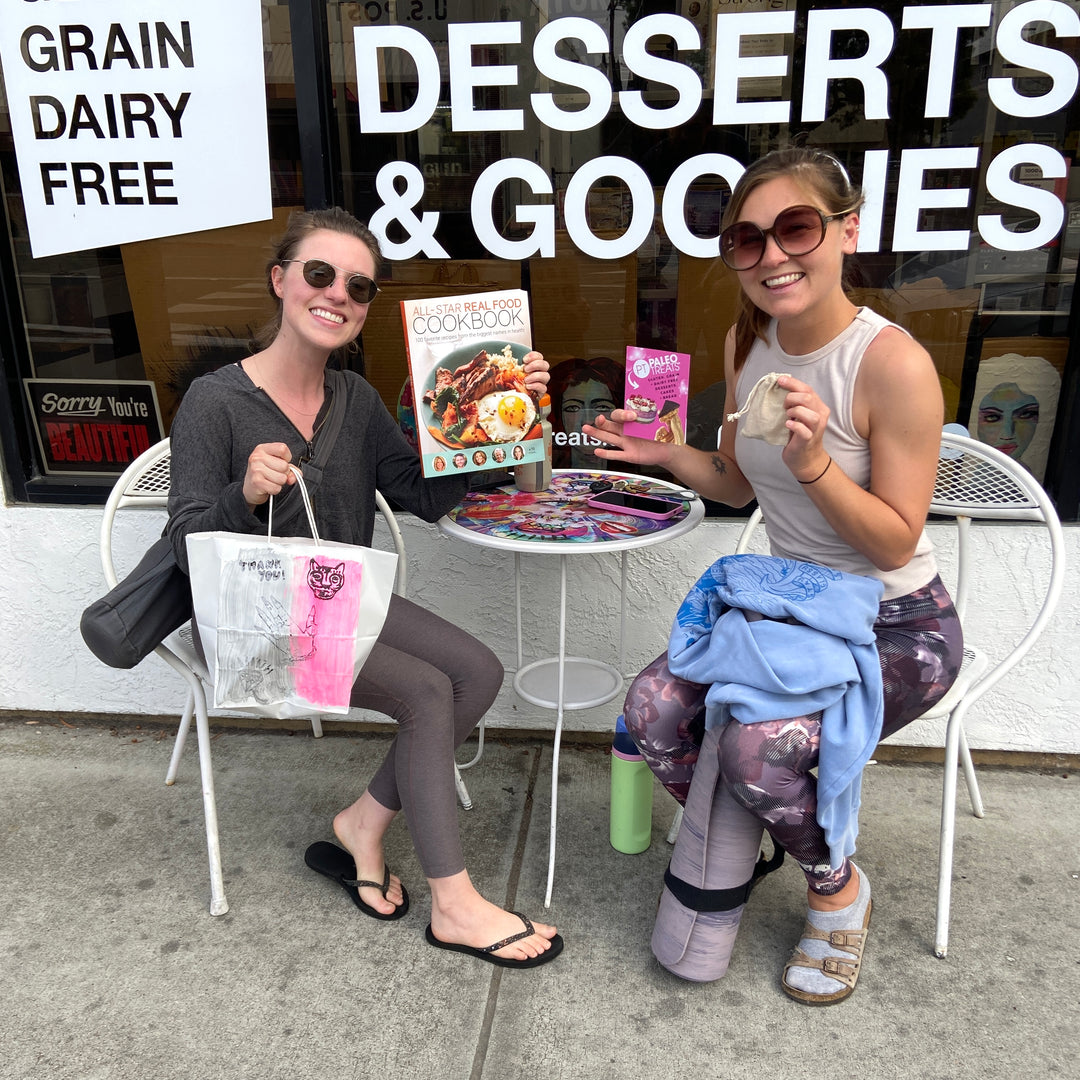 Ascb 2 smiling women with cookbook healthy recipes outside adams ave store.