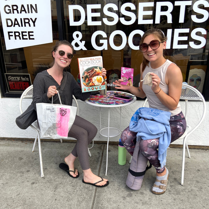 Ascb 2 smiling women with cookbook healthy recipes outside adams ave store.
