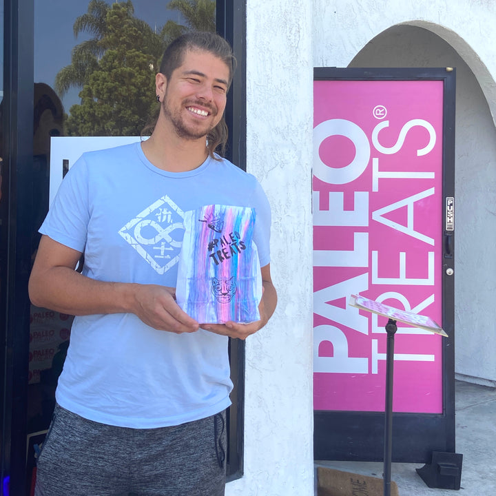 Baller bread smiling man with fresh keto bread in a bag in front of paleo treats shop.