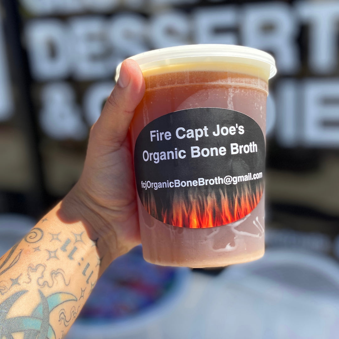 Bone broth tattoed arm holds up tub of fat cap bone broth by Paleo Treats.