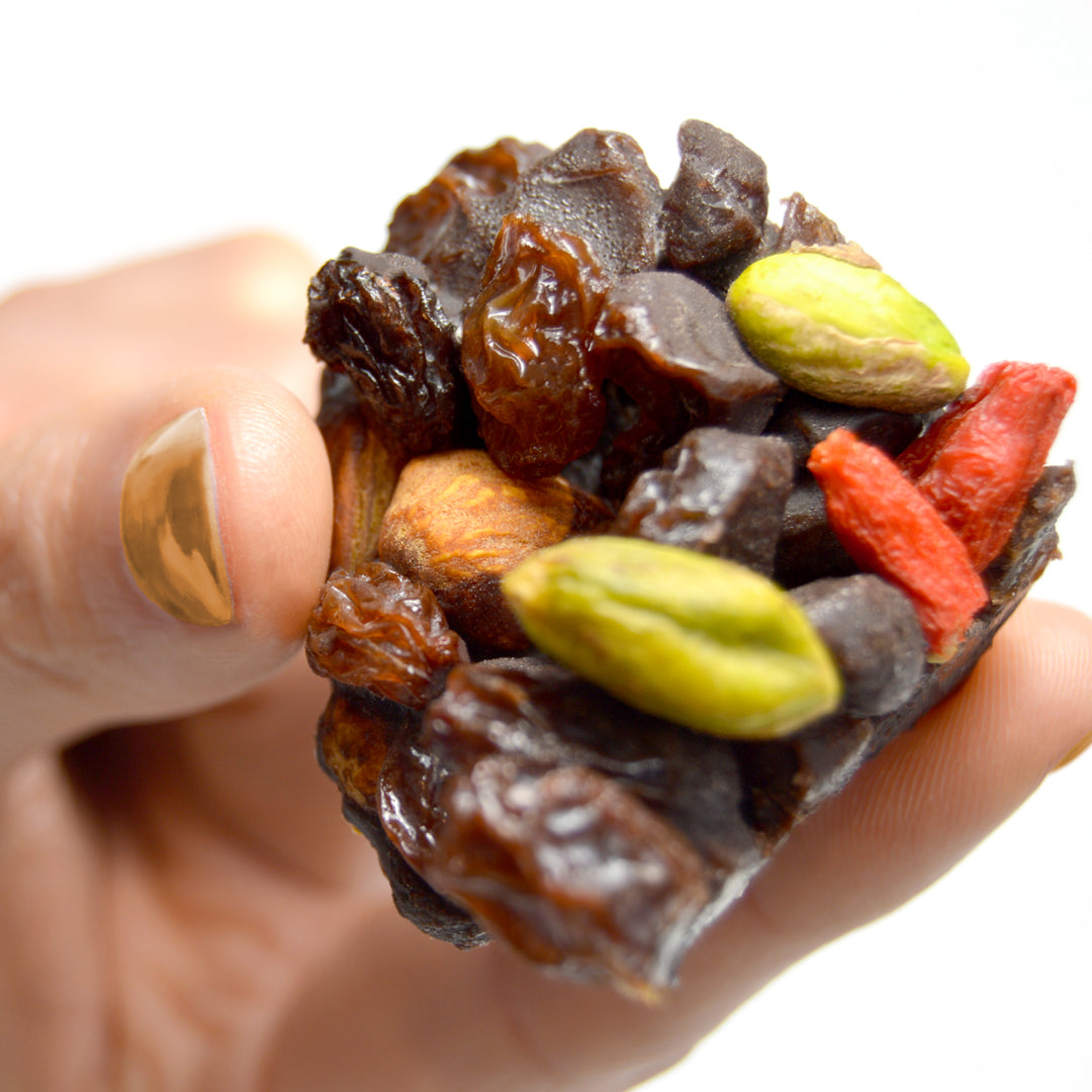 Piece of paleo chocolate fruit nut bar called cacao now by paleo treats held in womans hand.