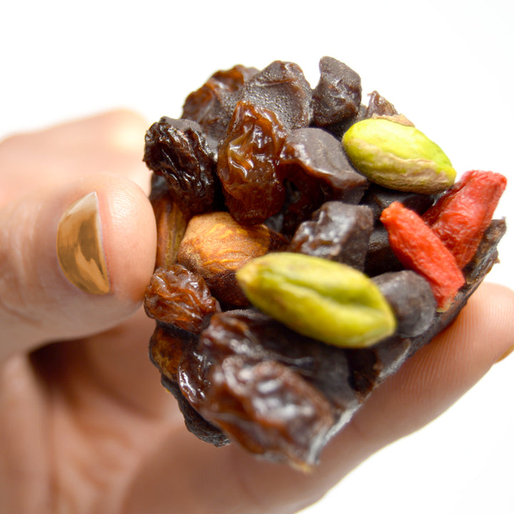 Piece of paleo chocolate fruit nut bar called cacao now by paleo treats held in womans hand.