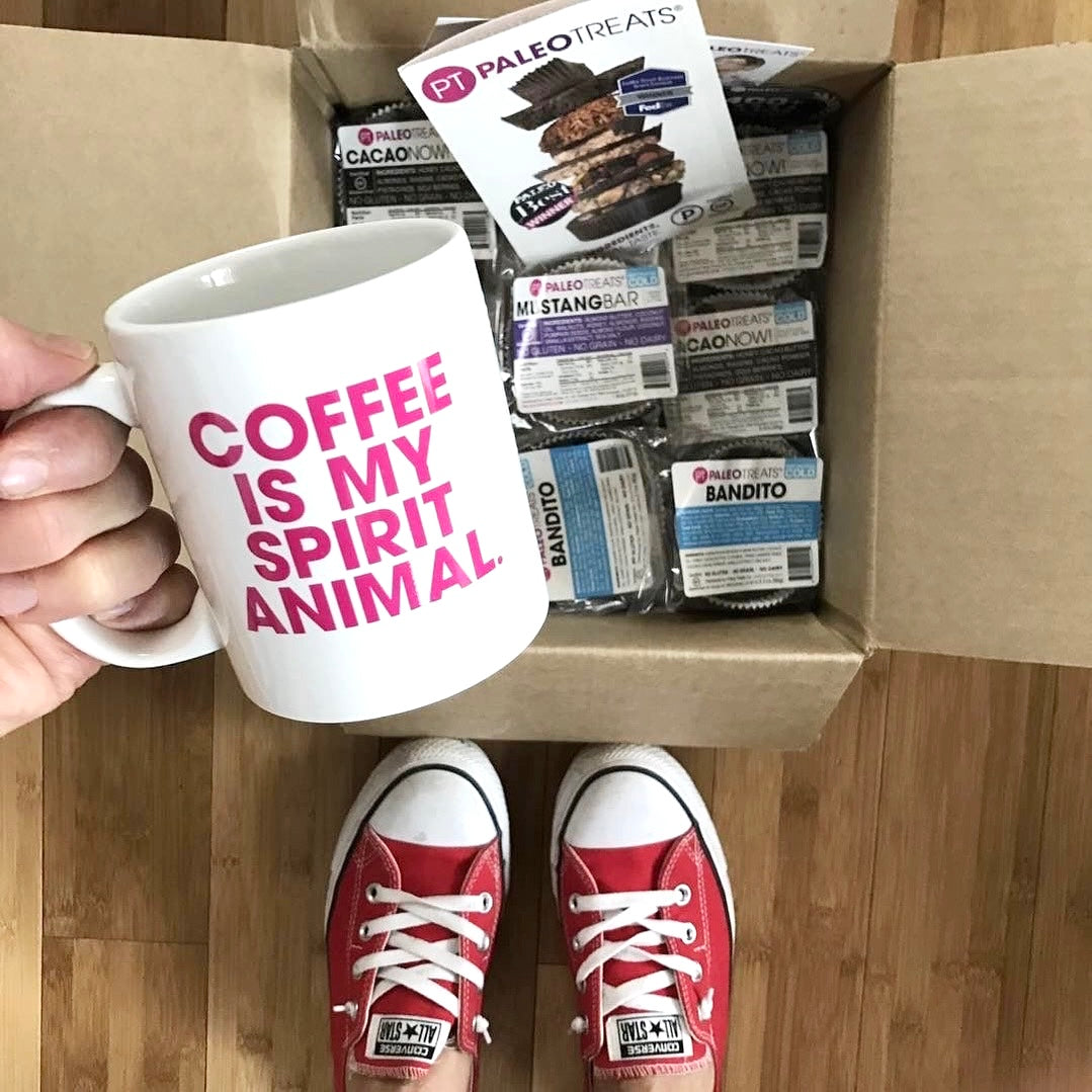Small stack sampler woman holds mug over opened shipped box of paleo treats.