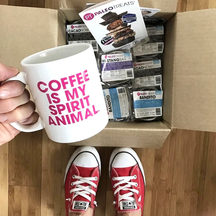 Small stack sampler woman holds mug over opened shipped box of paleo treats.