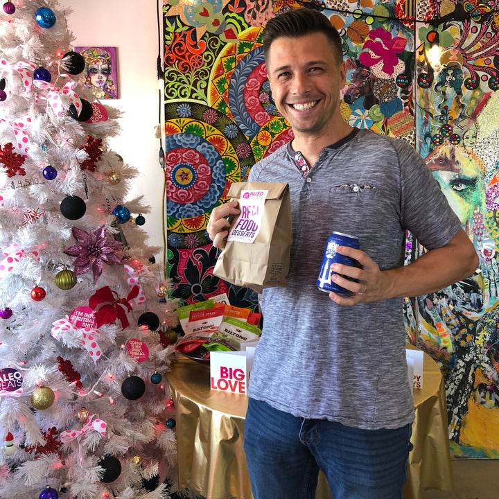 Smiling man holding bag with real food desserts sticker and can of trident cold brew coffee.