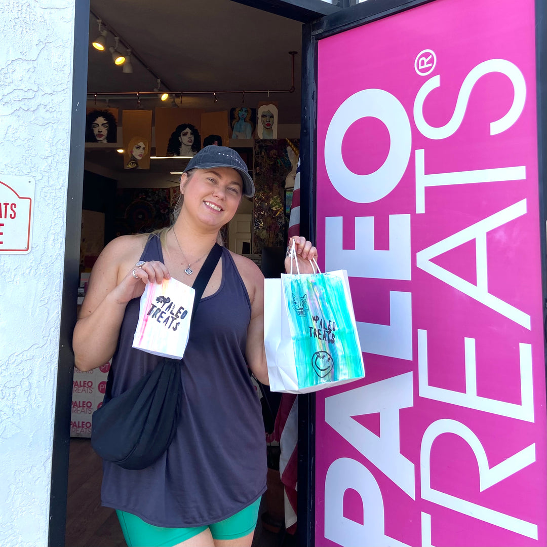 Woman at door of paleo treats with two bags of desserts.
